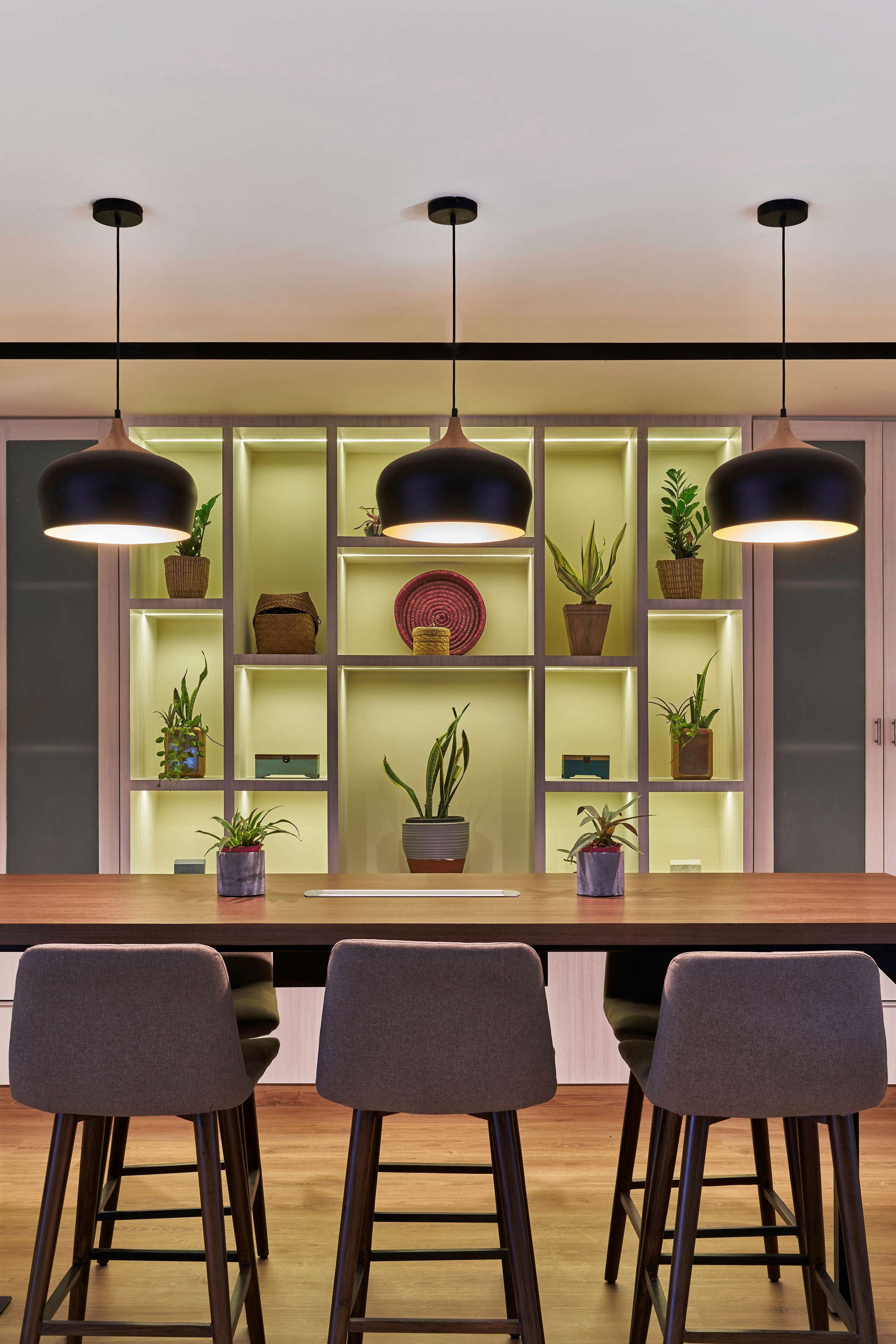 Una cocina moderna con tres taburetes de bar, iluminación colgante y un estante empotrado para plantas.