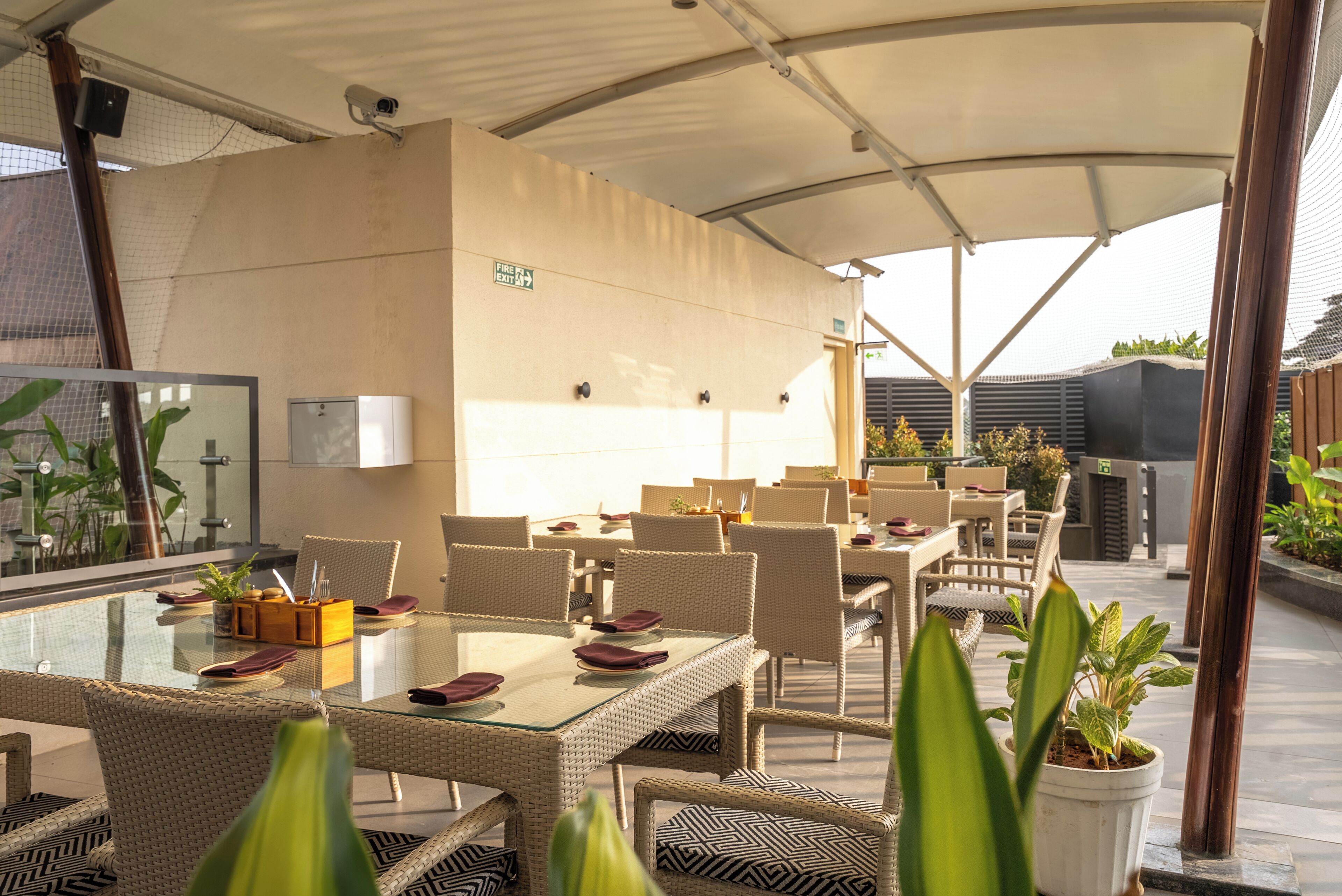 An outdoor dining area with wicker furniture and glass tables, a covered seating area, and potted plants.