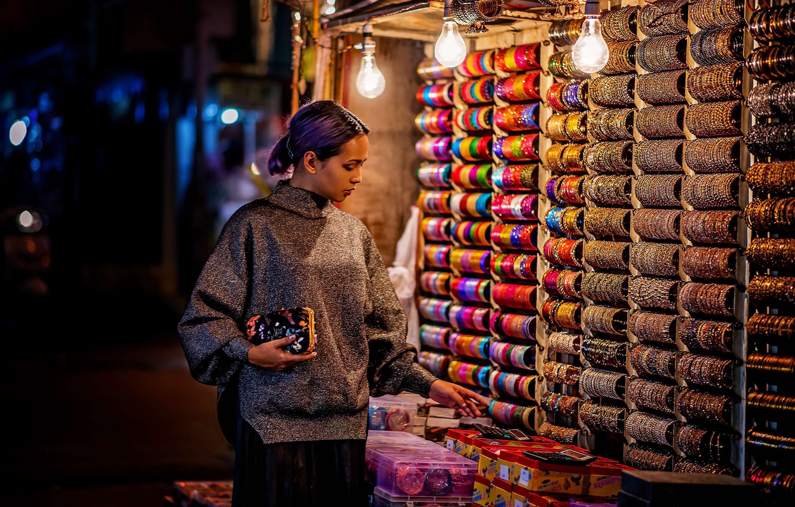 A person at a market stall with colorful bangles and light bulbs.