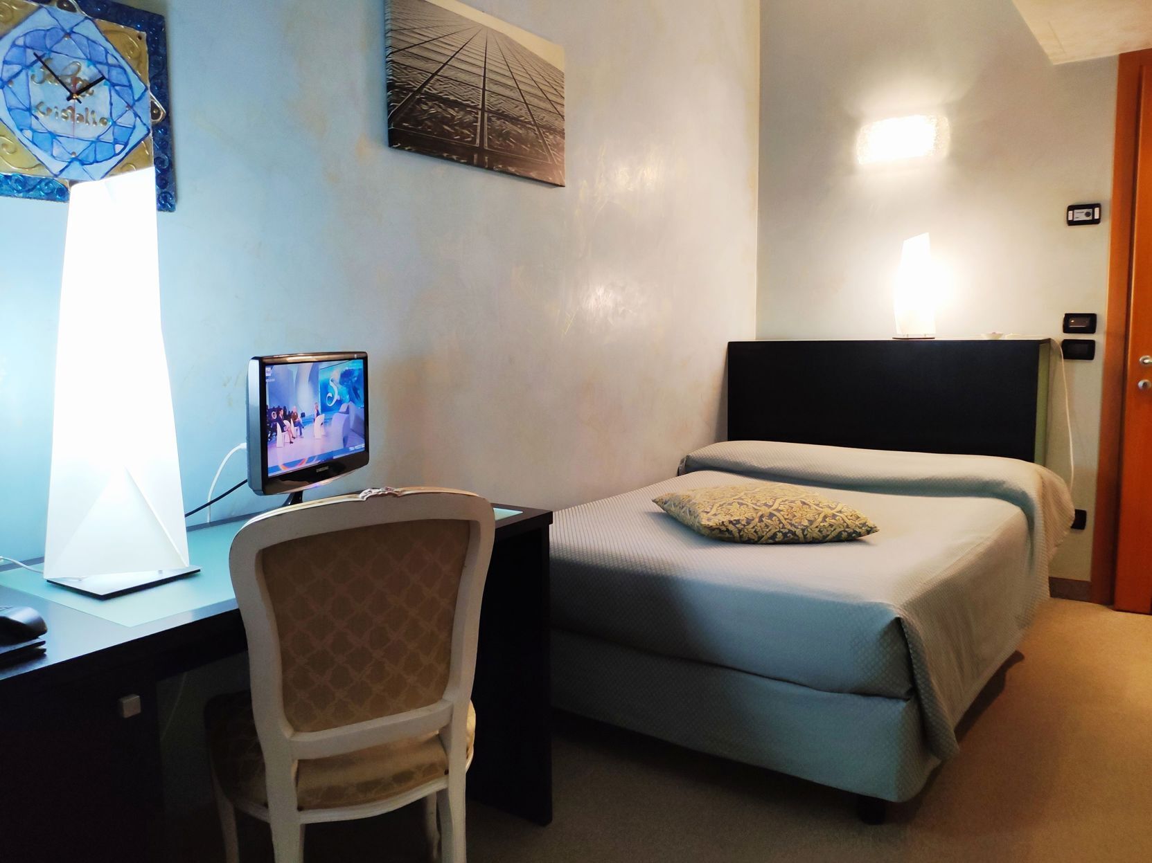 Een hotelkamer met een bed, een bureau met een computer, een stoel en een wandklok.