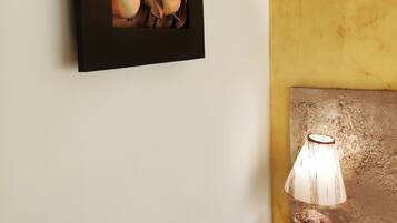 A framed artwork of autumn leaves on a white wall, a rustic lamp on a wooden table, and a textured wall.