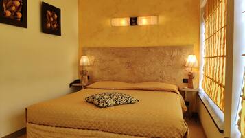 Una camera d'albergo con un letto grande, due lampade sui comodini, una testiera e una finestra con persiane.