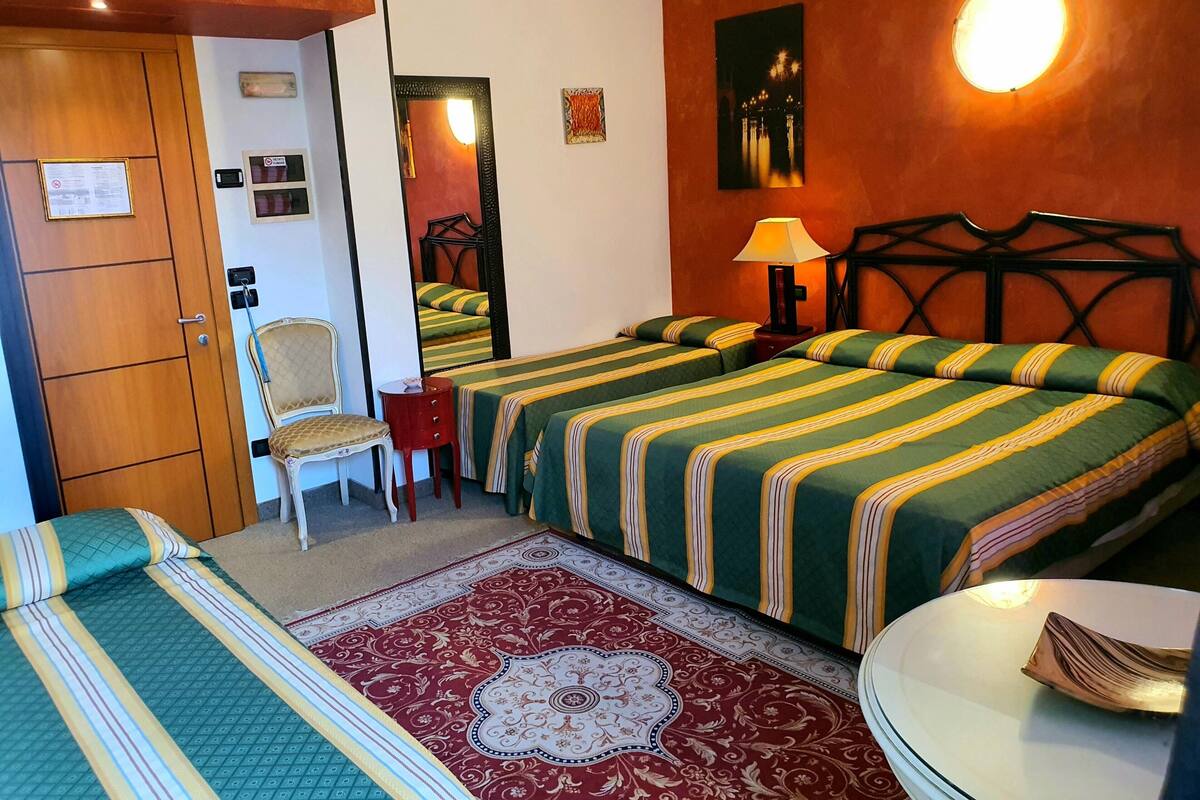 Ein Hotelzimmer mit zwei Betten, einem Sessel, einem kleinen Tisch und einem roten Teppich mit Muster.