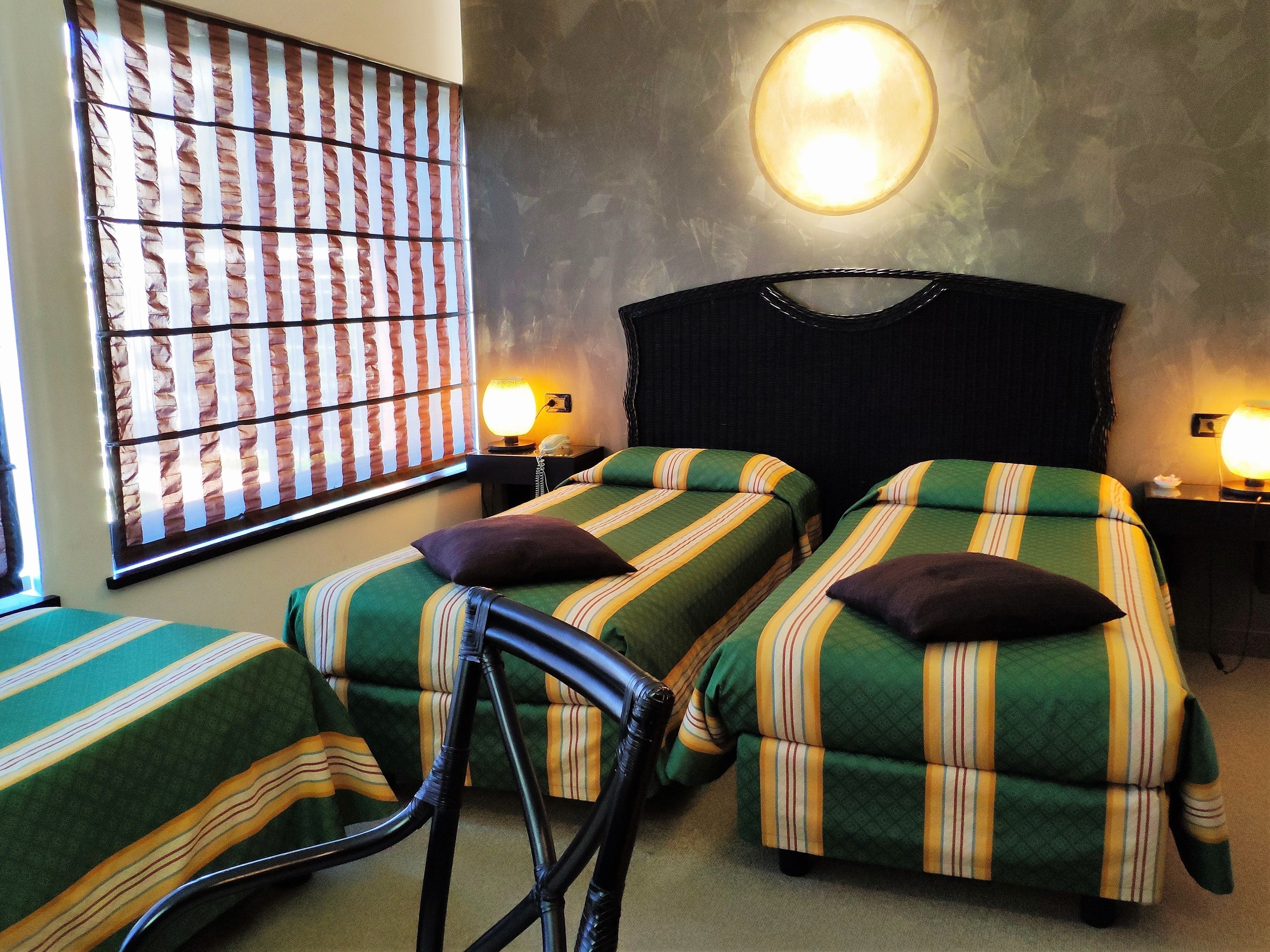 A room with two single beds, a chair, a wall-mounted lamp, and a window with striped curtains.