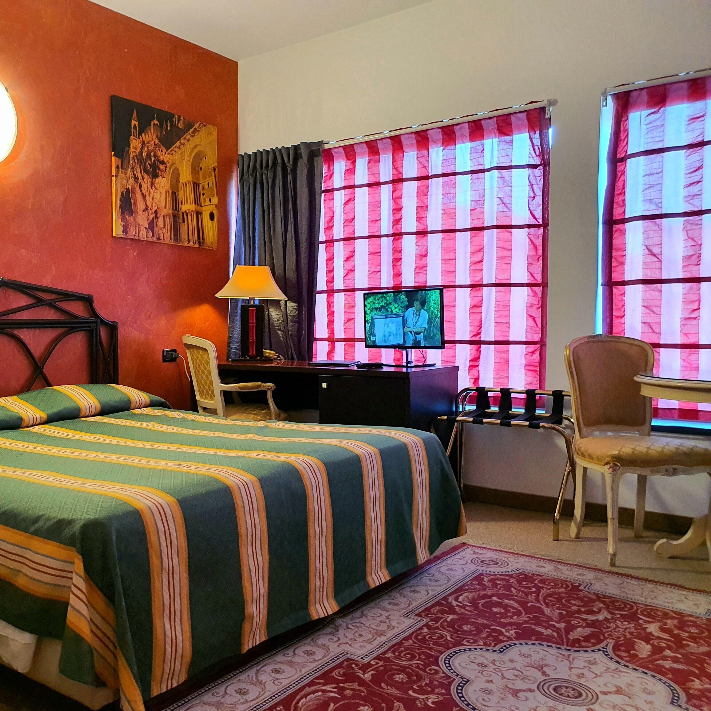 A hotel room with a bed, desk, chair, TV, and a painting on the wall.