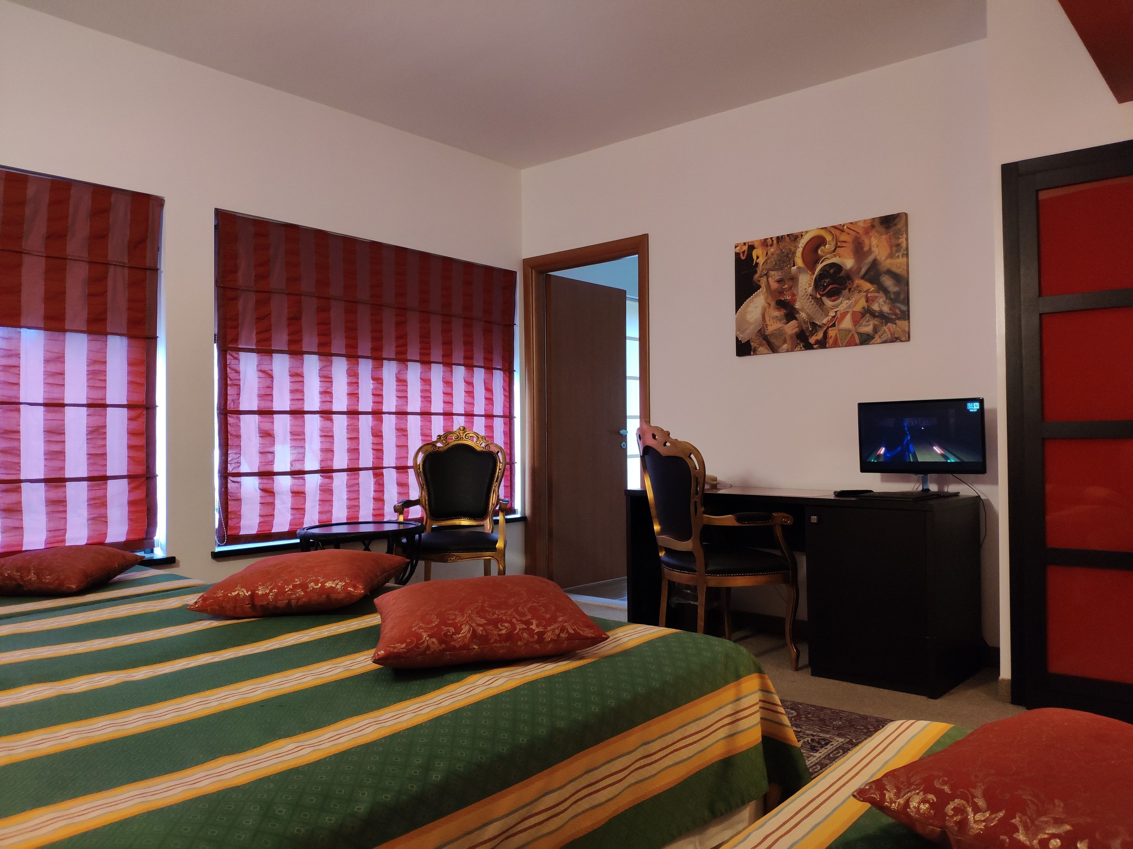 A hotel room with a bed, a desk, a television, and a painting on the wall.
