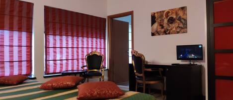 A hotel room with a bed, a desk, a television, and a painting on the wall.