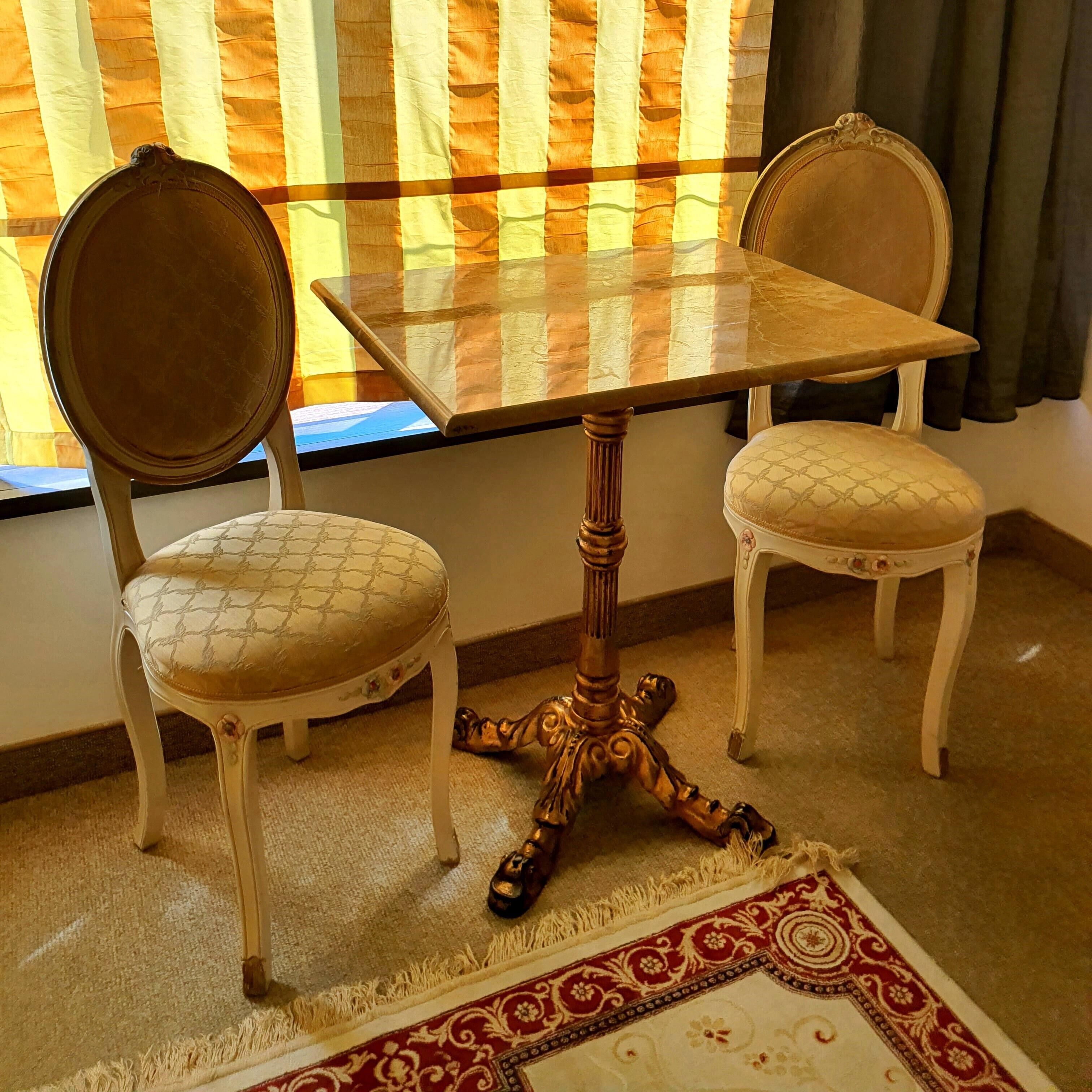 A dining table with two chairs, a patterned rug, and a window with curtains.
