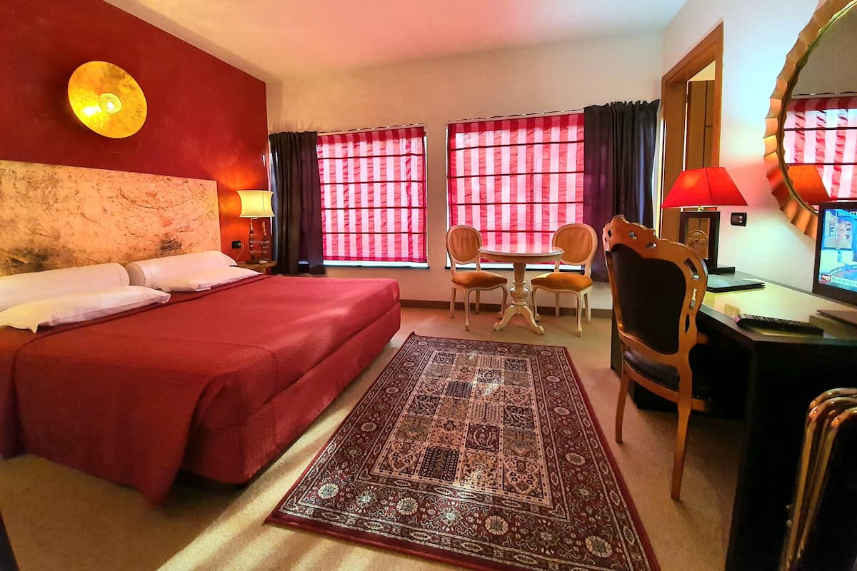 Ein Hotelzimmer mit einem großen Bett, einem Schreibtisch mit Computer, zwei Stühlen, einem kleinen Tisch und einem dekorativen Teppich.