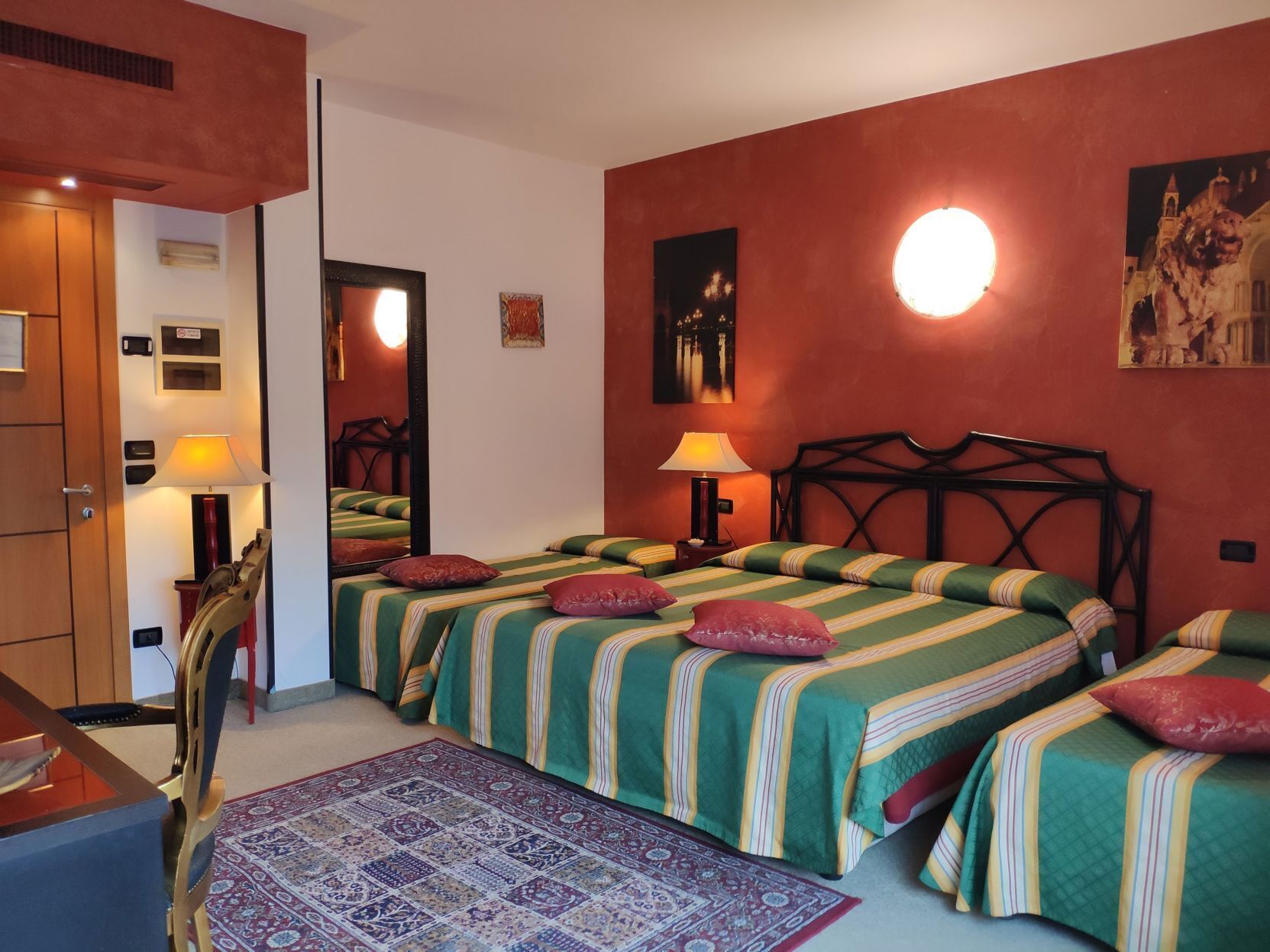A hotel room with two beds, a desk, a chair, a mirror, a lamp, and a rug.
