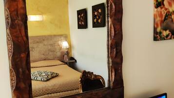 A bedroom with a large mirror, a bed with a patterned pillow, a bedside lamp, and a television on a stand.