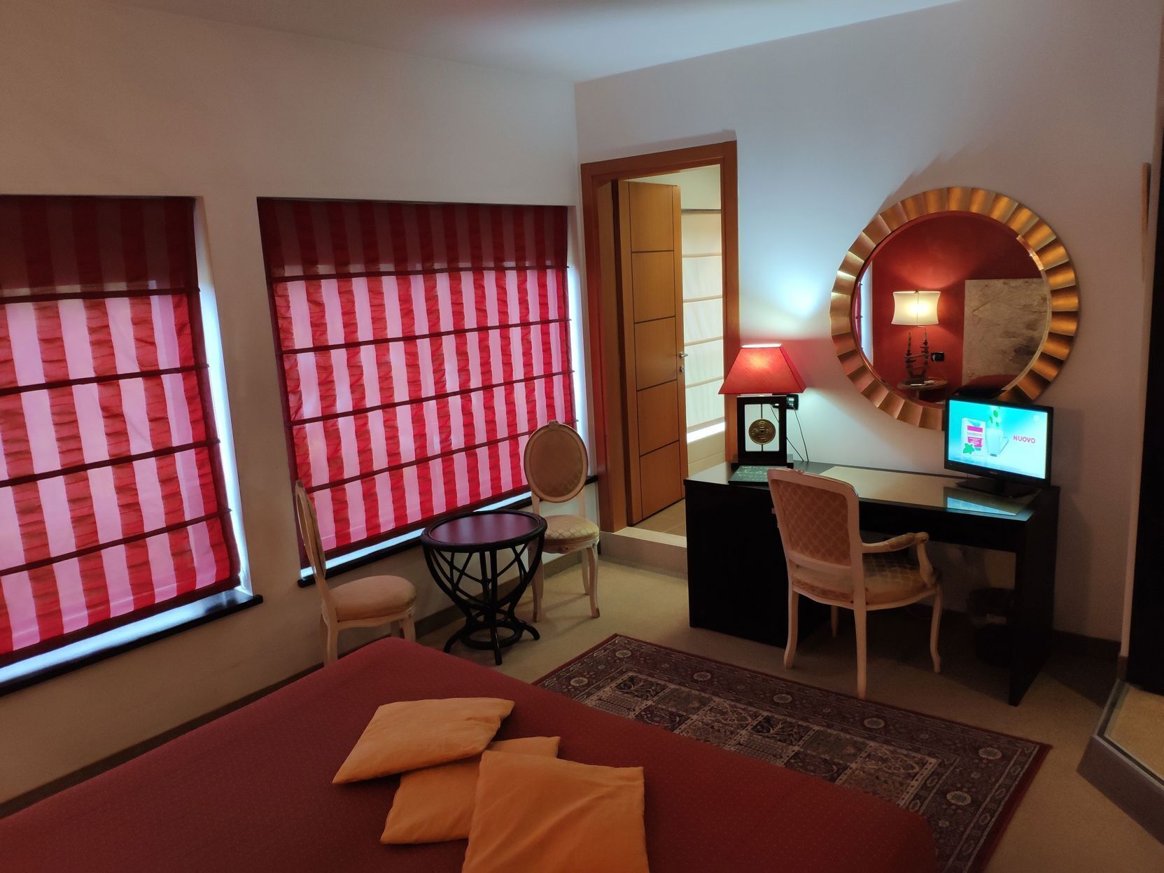 Een hotelkamer met een bed, een bureau met een computer, een stoel, een lamp en een grote spiegel.