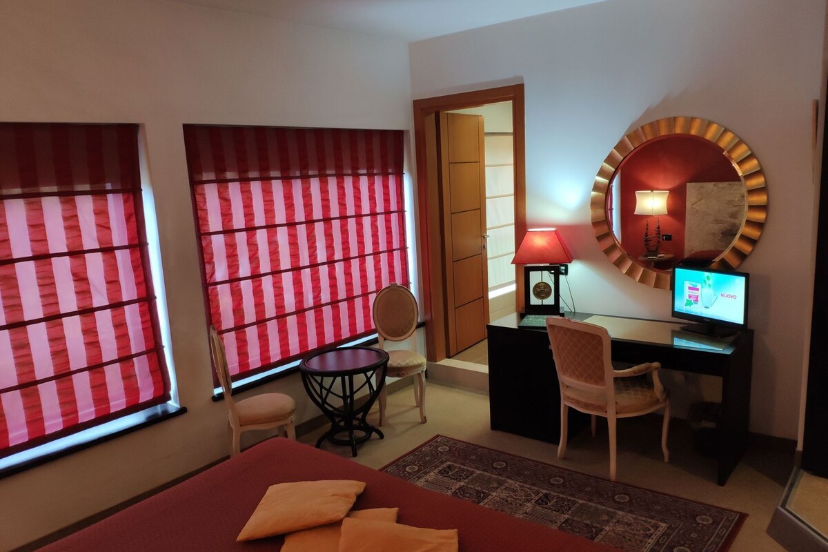 Een hotelkamer met een bed, een bureau met een computer, een stoel, een lamp en een grote spiegel.