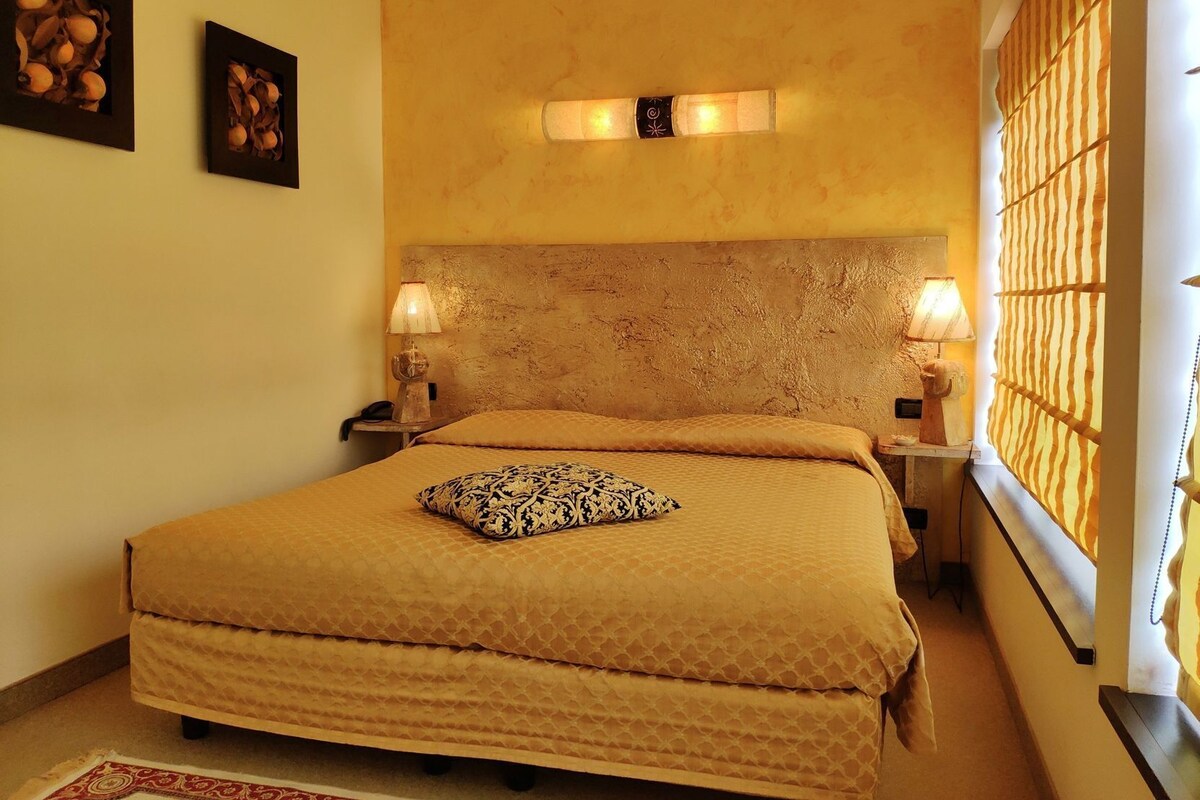 Een kamer met een groot bed, twee bedlampen, een hoofdeinde en een raam met jaloezieën.