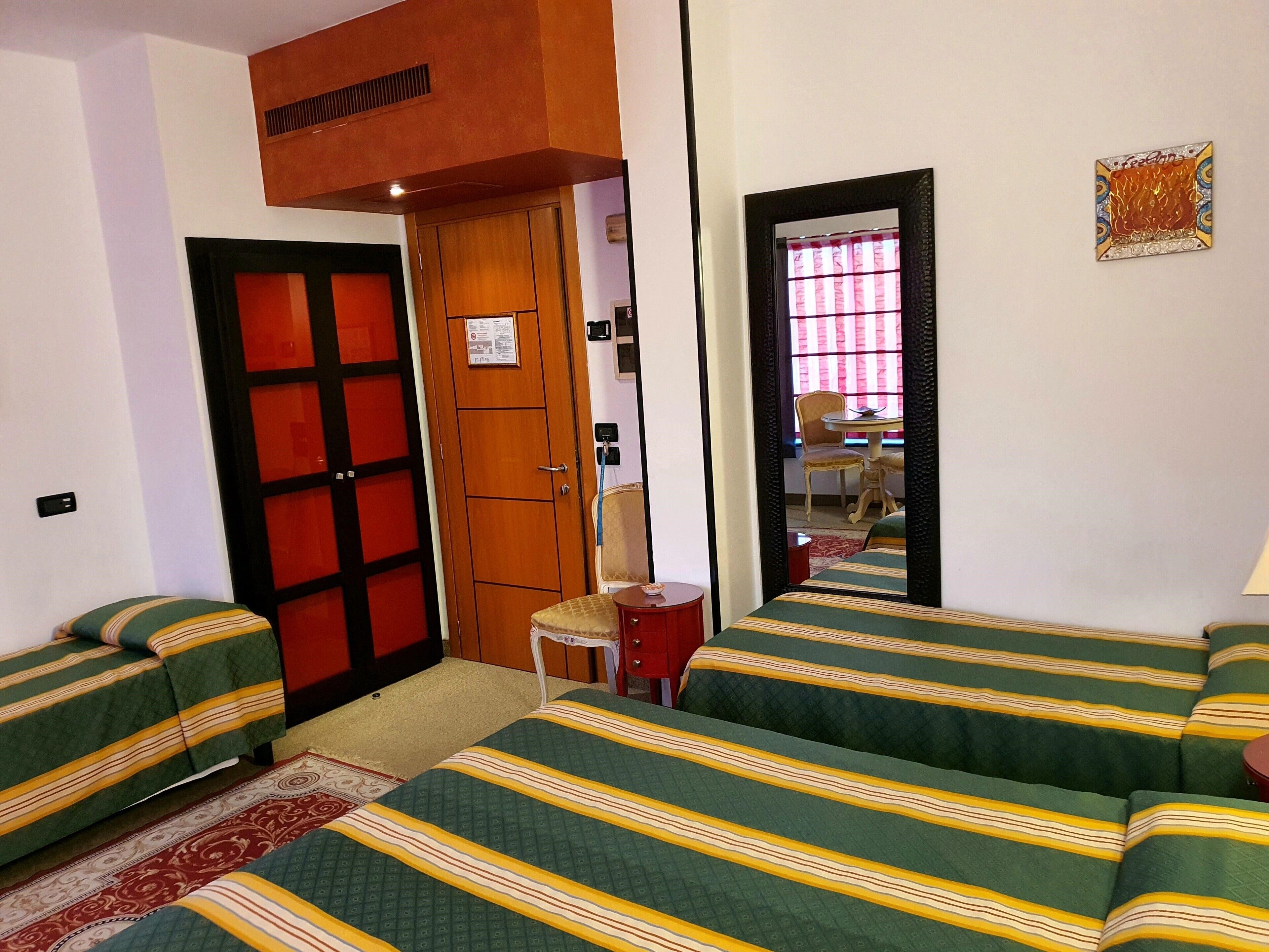 Una camera d'albergo con due letti singoli, un armadio in legno, un tavolino con una sedia e uno specchio a parete.