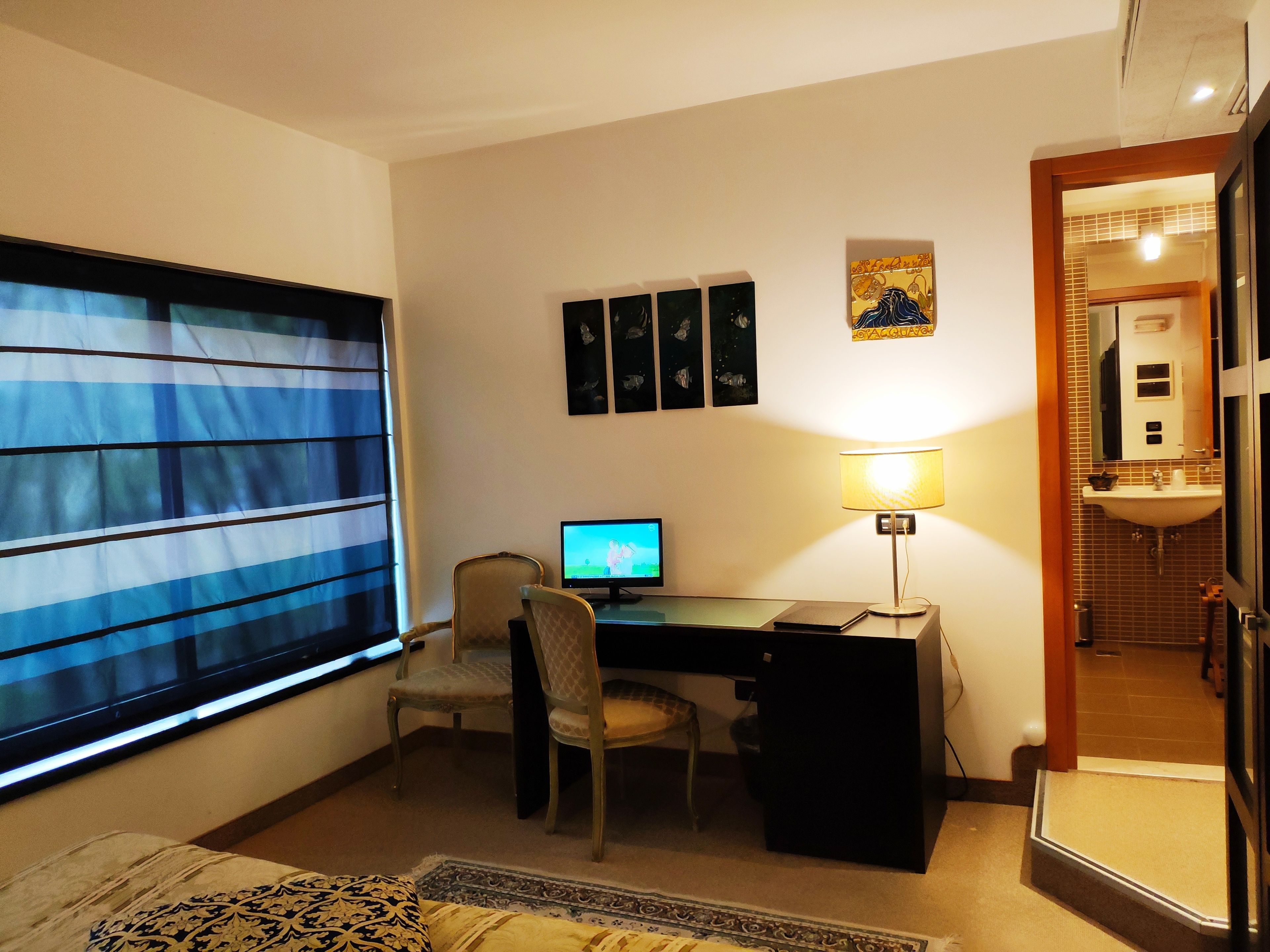 A room with a desk, chair, computer, and a window with blinds.
