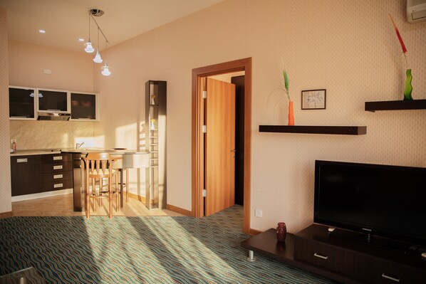 Una habitación de hotel moderna con una zona de cocina, una mesa de comedor con sillas, un televisor de pantalla plana y una alfombra estampada.