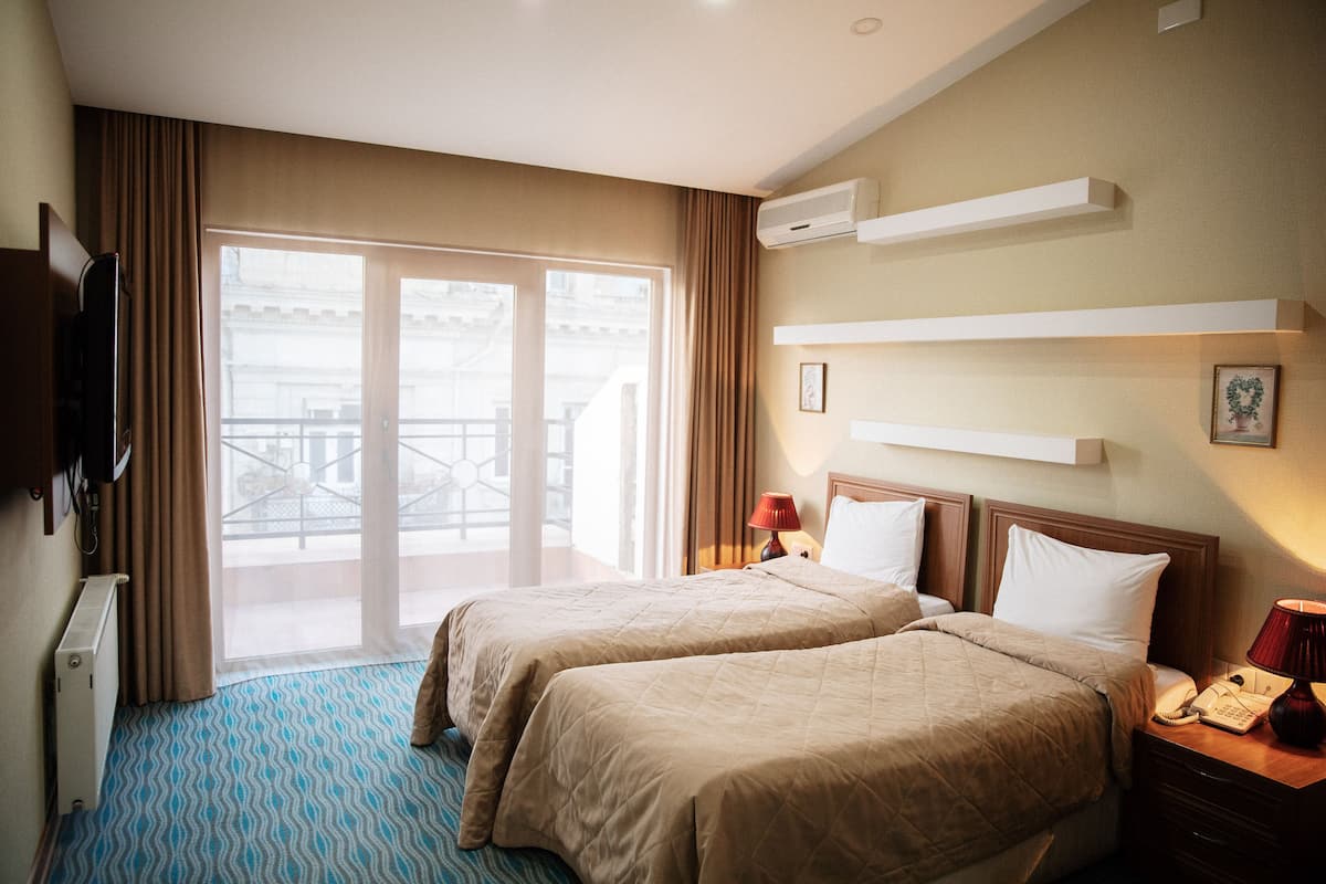 A hotel room with two beds, a television, a desk with a telephone, and a view of the outside balcony.