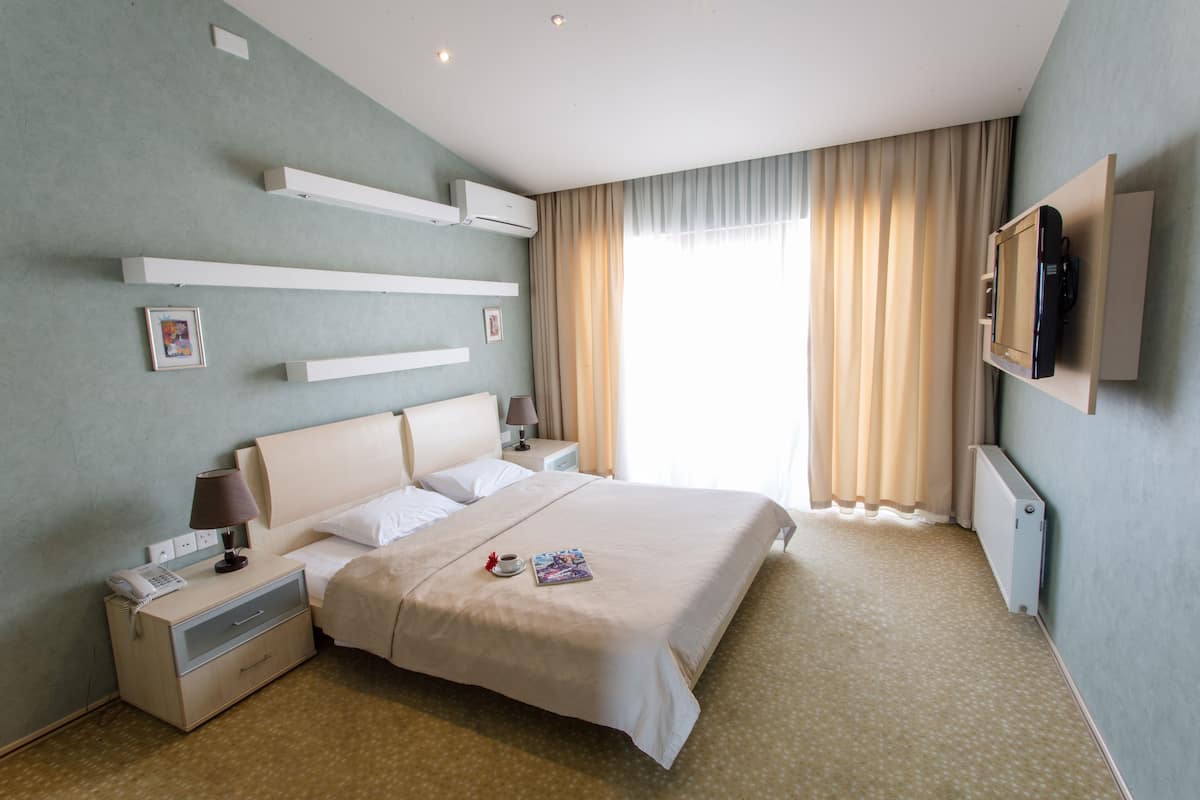 A hotel room with a large bed, bedside tables, a TV mounted on the wall, and a window with curtains.