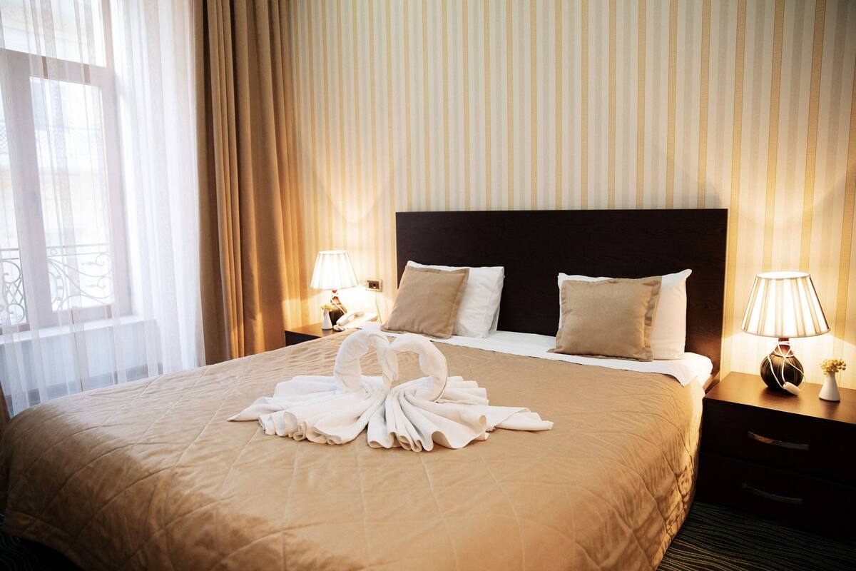 A hotel room with a large bed, two bedside tables, and a window with curtains.