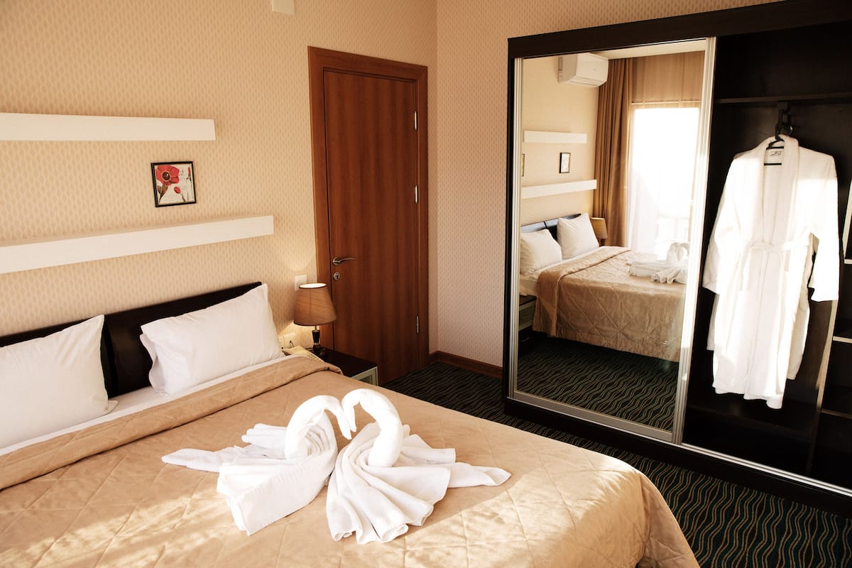 A hotel room with a bed, a mirror, a robe, and a towel arrangement.