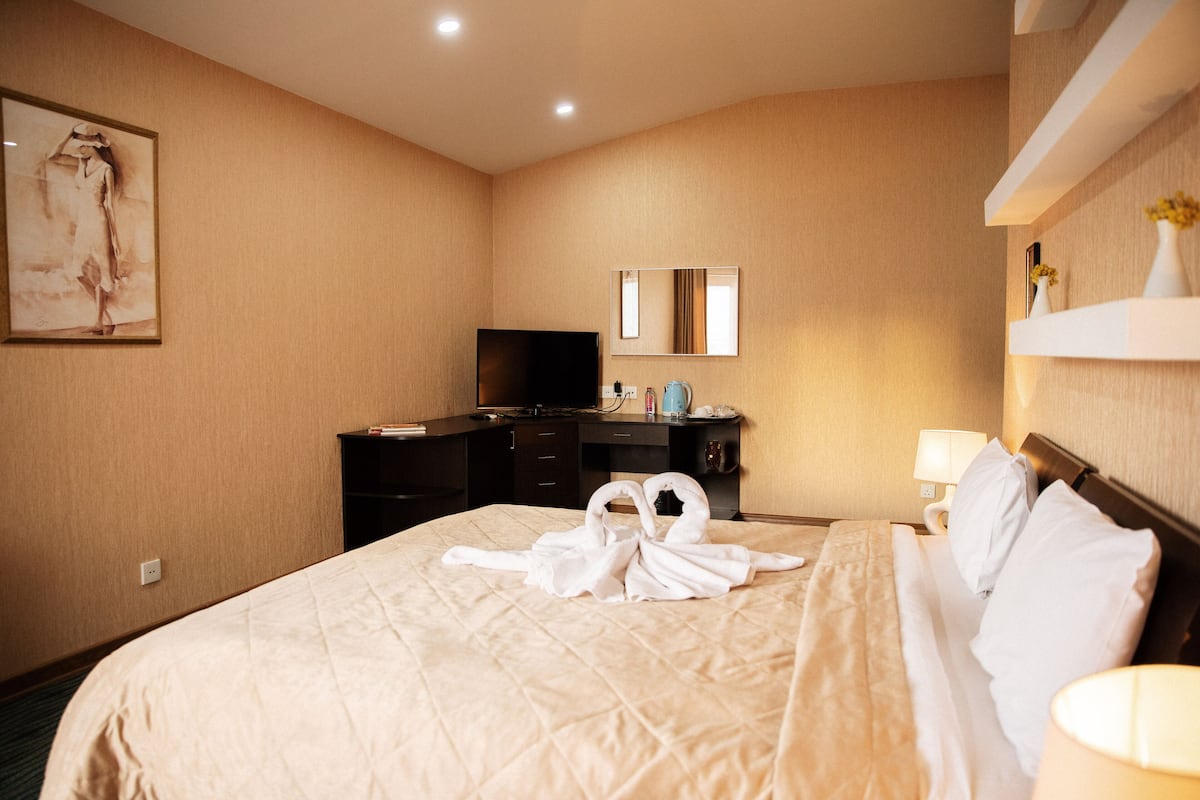 A hotel room with a large bed, a flat-screen TV, a dresser, and a mirror on the wall.