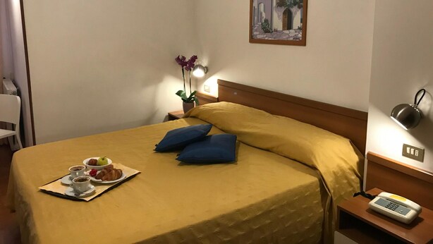 Een hotelkamer met een bed, een nachtkastje met een lamp, een schilderij aan de muur en een dienblad met eten en drinken op het bed.
