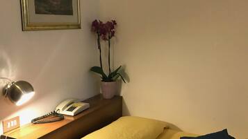 A hotel room with a bed, a bedside table with a lamp, a phone, and a framed picture on the wall.