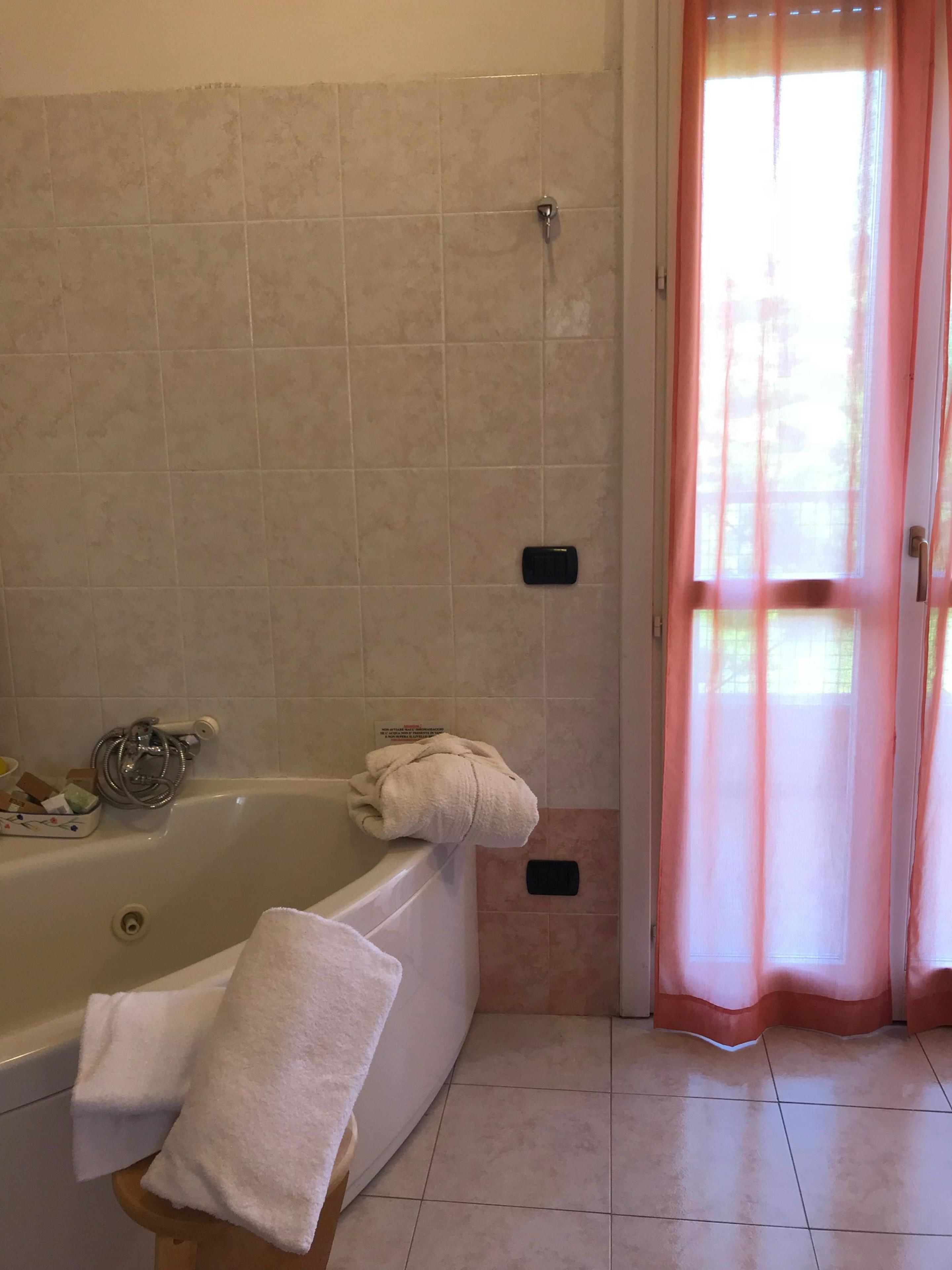 Un baño con bañera, cabezal de ducha, toallero y una ventana con cortinas.