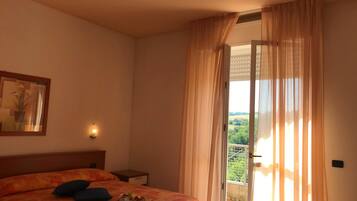 A hotel room with a bed, a nightstand, a painting, and a balcony with curtains.