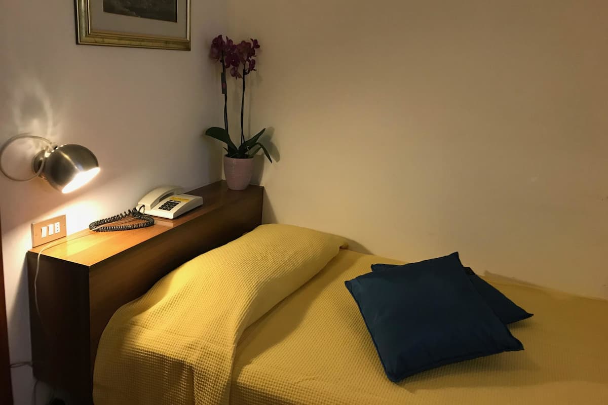 Un lit bien fait, avec une couverture jaune et un oreiller bleu, une lampe de chevet, un téléphone et une plante en pot sur une table de chevet en bois.