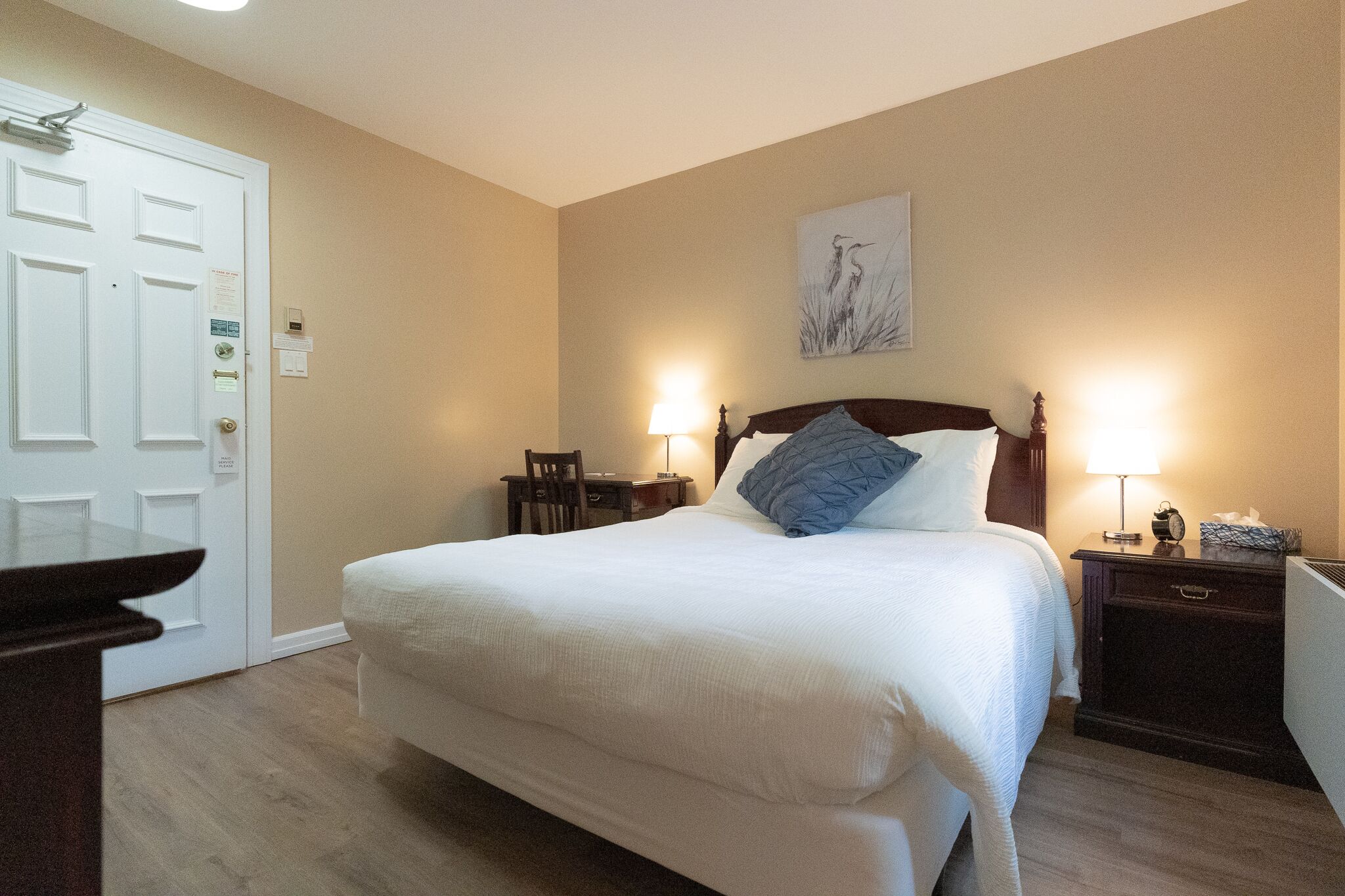 A neatly arranged bedroom with a large bed, bedside tables with lamps, a desk, and a chair.