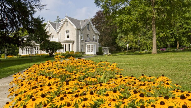 Un edificio de piedra grande con fachada simétrica, una entrada central y un césped cuidado con flores amarillas.