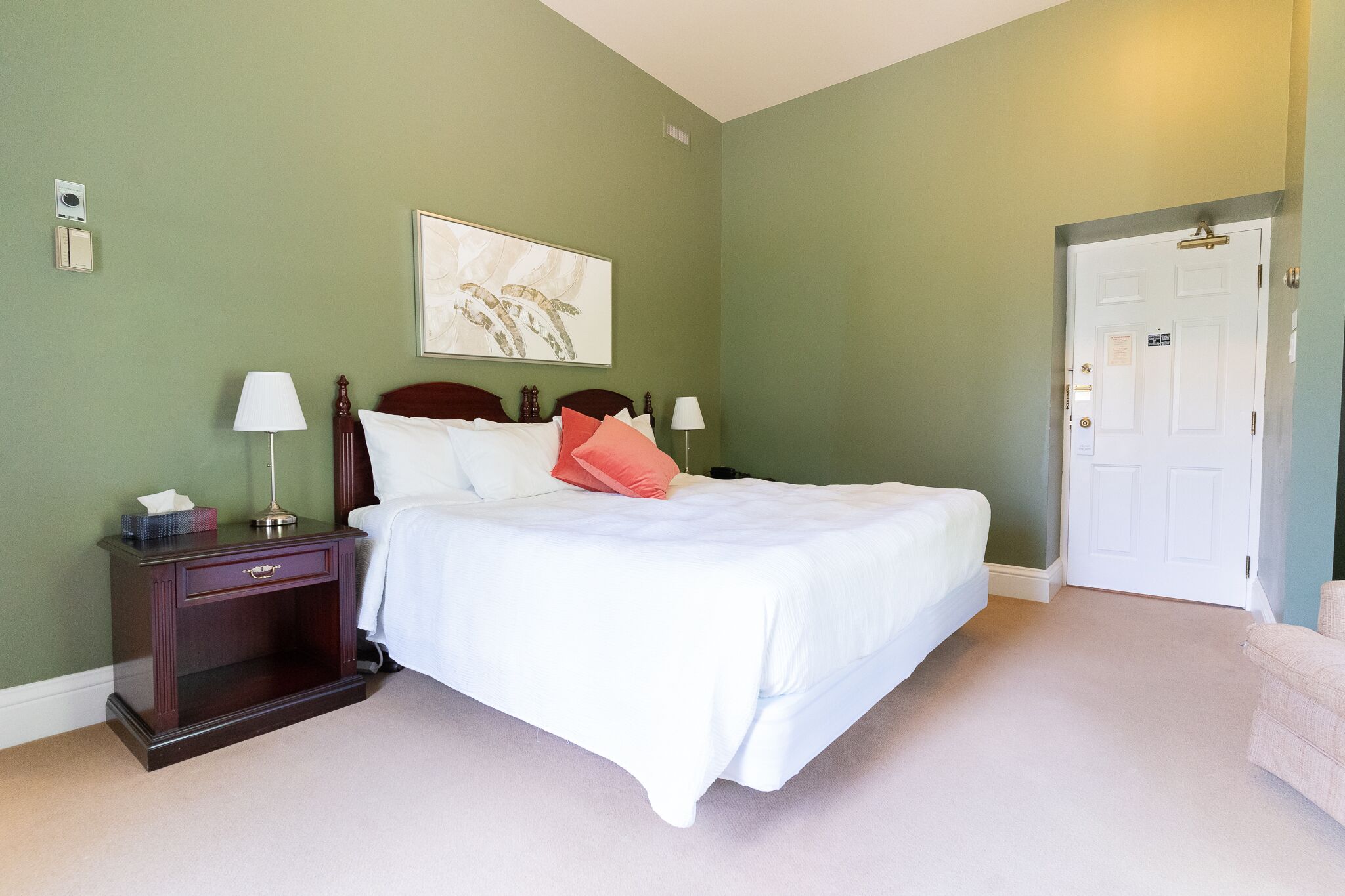 A neatly arranged bedroom with a bed, bedside tables, a nightstand, and a door.