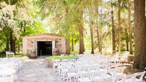 Salón de bodas al aire libre con suelo de piedra, sillas blancas y entrada de un edificio de piedra.