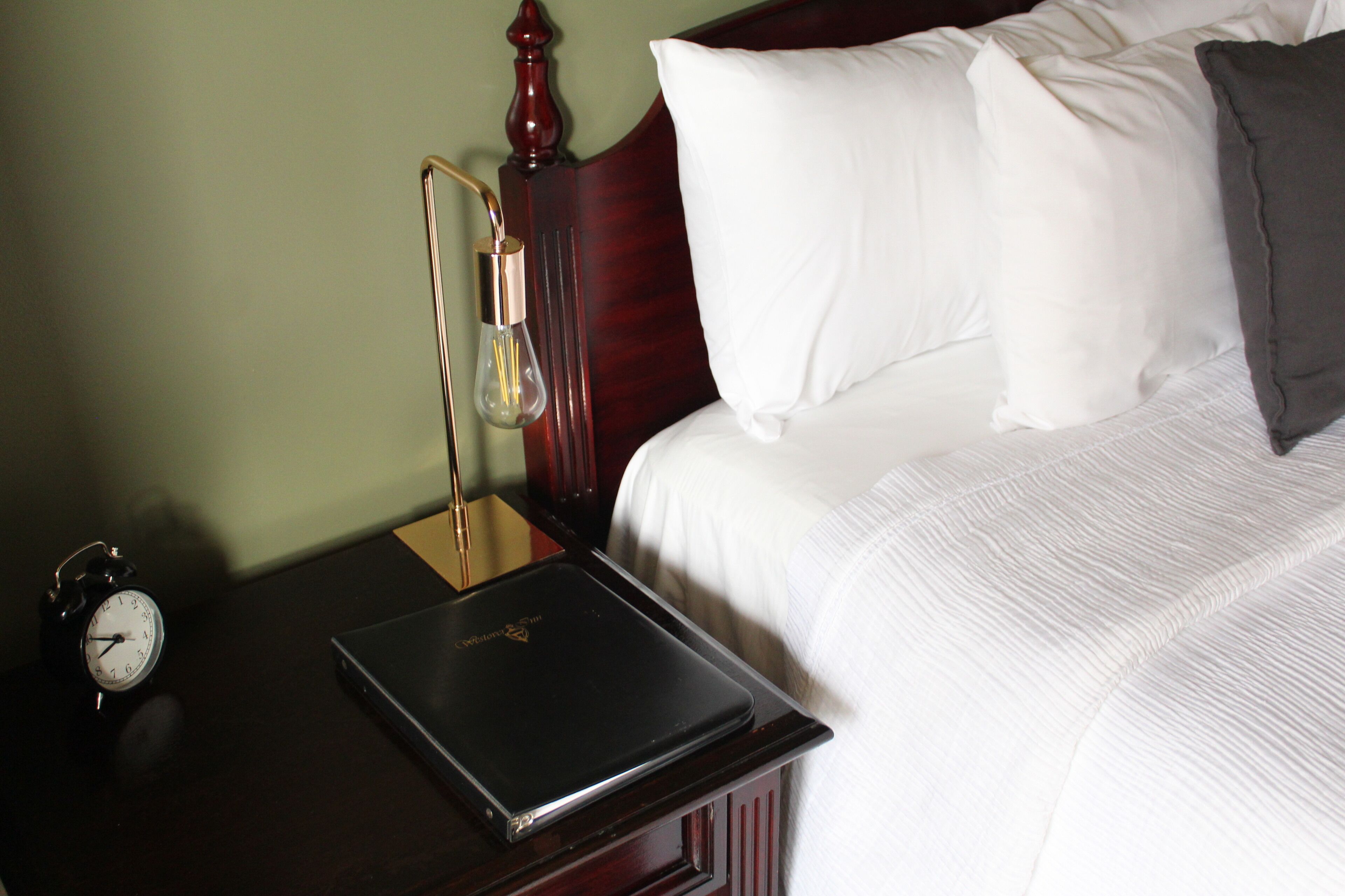 A neatly made bed with white and gray pillows, a wooden headboard, and a laptop on a bedside table.