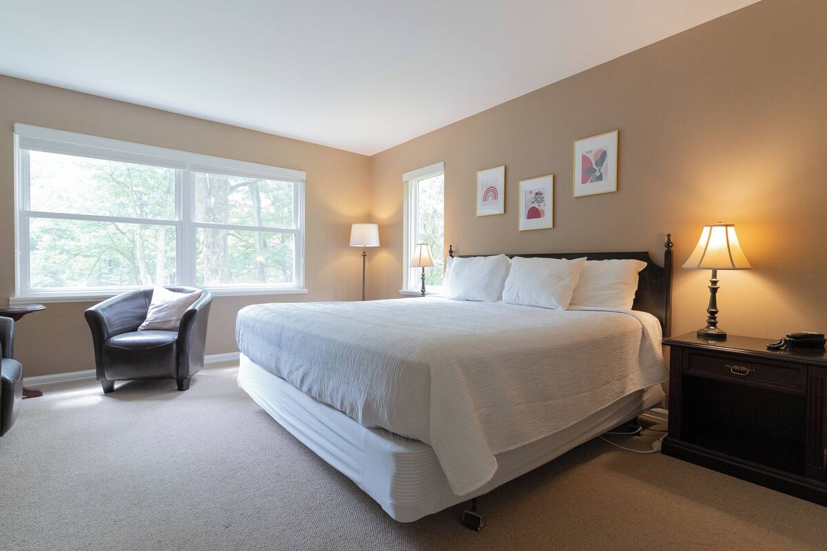 A bedroom with a large bed, two bedside lamps, a chair, and a nightstand.