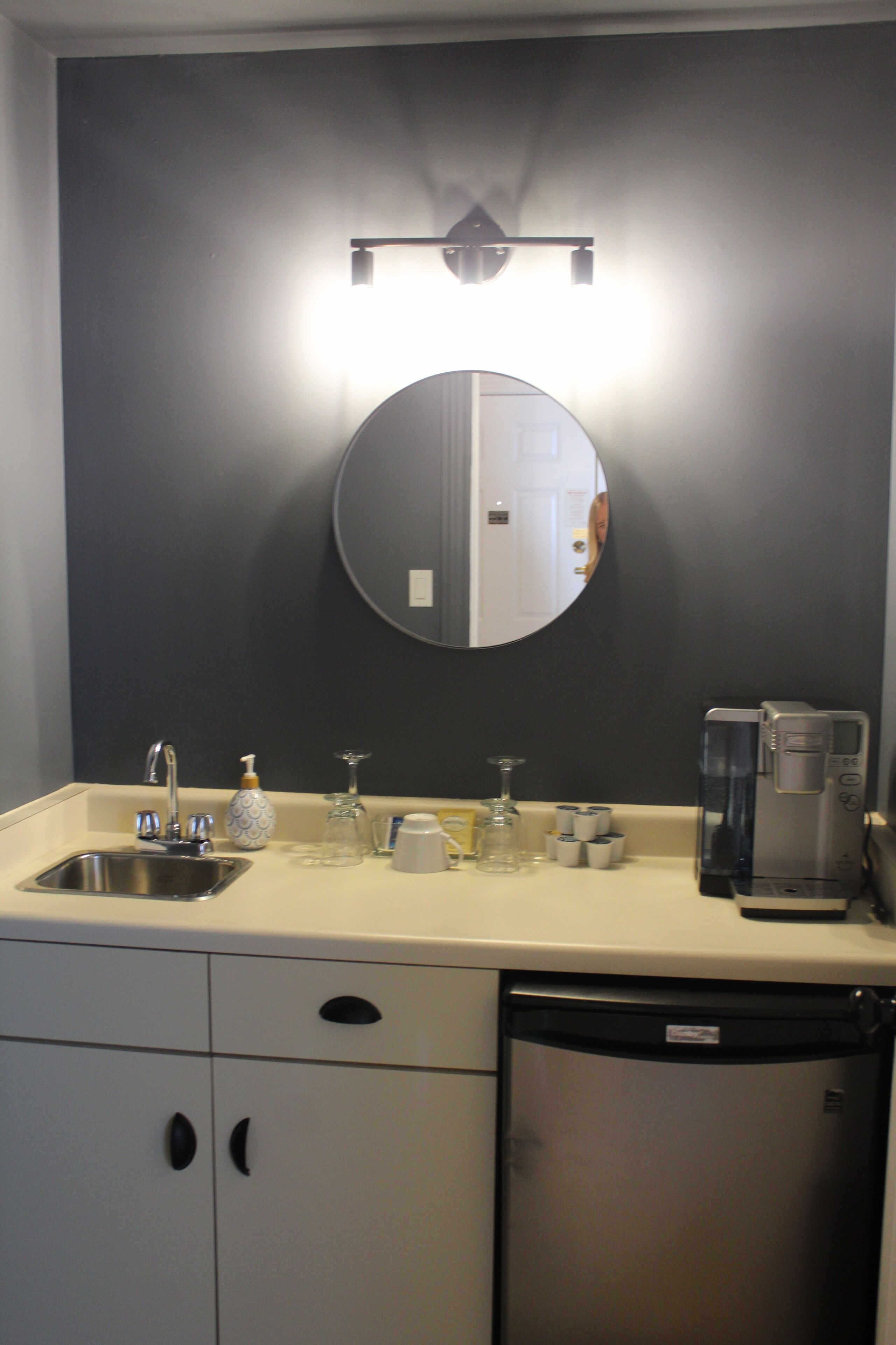 Un baño moderno con lavabo, espejo y cafetera.