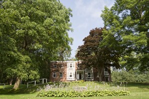 A historic building with a brick facade, large windows, and a well-maintained garden with a bench and flowering plants.