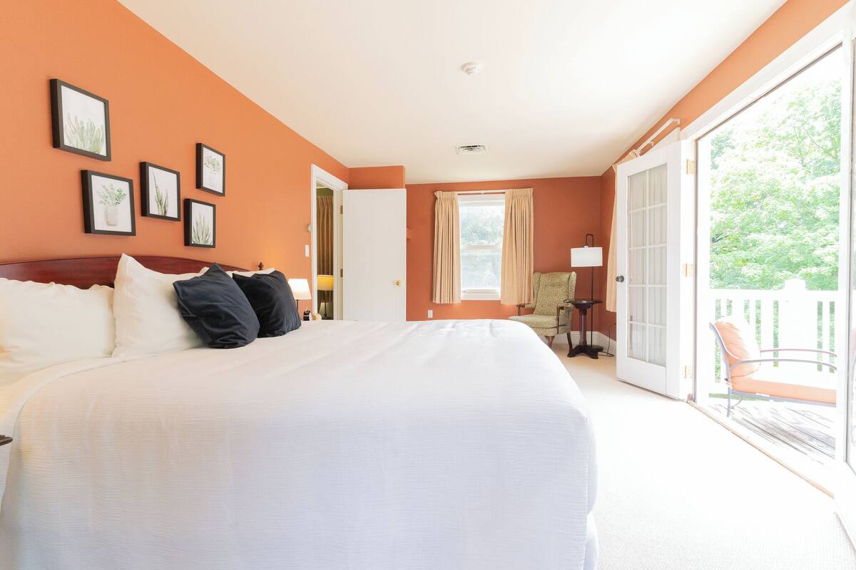 A bedroom with a large bed, a door leading to a balcony, and framed pictures on the wall.