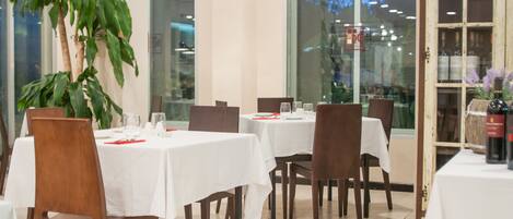 Un restaurante con mesas dispuestas para comer, ventanas amplias y una planta en maceta.