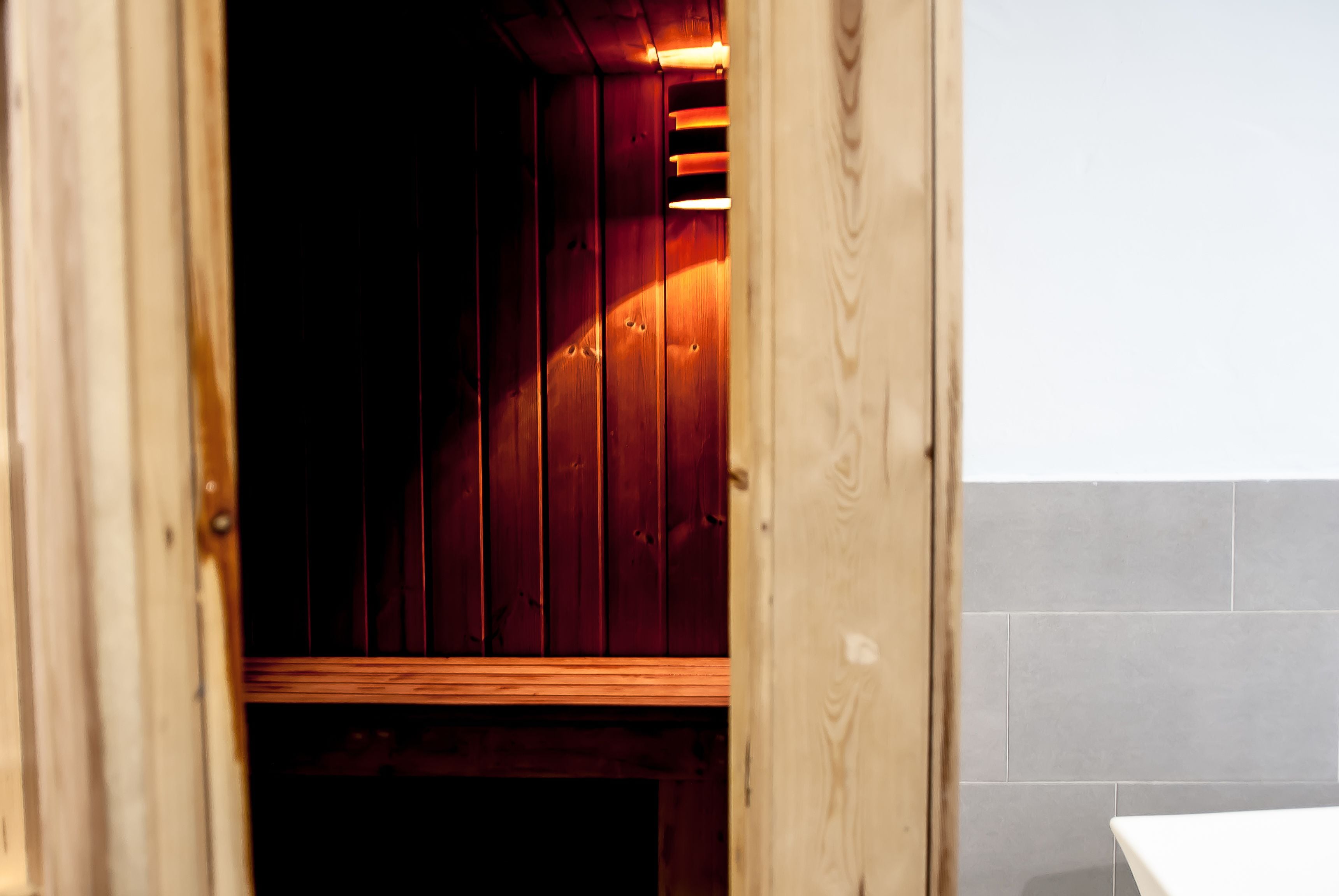 Un sauna en bois avec un banc, un mur carrelé et un cadre de porte en bois.