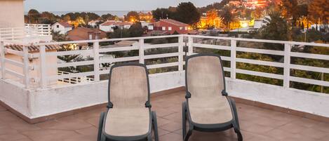 Two chairs on a balcony with a view of a hillside town at dusk.