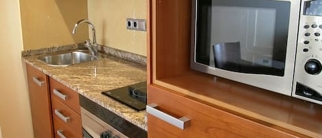 Cocina compacta con lavabo, estufa, microondas y armarios de madera.