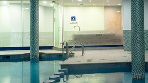 Una piscina interior con paredes de vidrio transparente, suelo de baldosas y el logotipo de 'JACUZZI'.