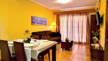 Un comedor con una mesa dispuesta para cuatro personas, un sofá, una lámpara y un televisor sobre un soporte.