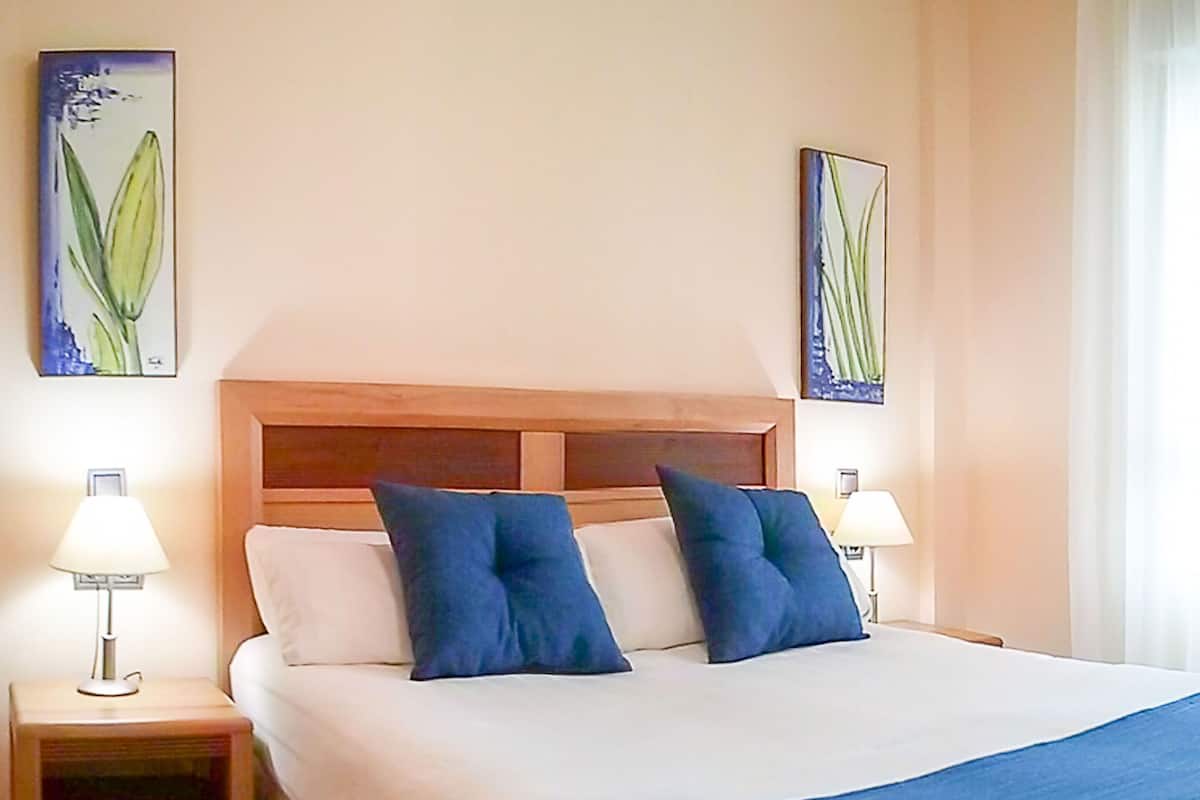 A neatly made bed with a wooden headboard, two bedside tables with lamps, and two wall-mounted paintings.