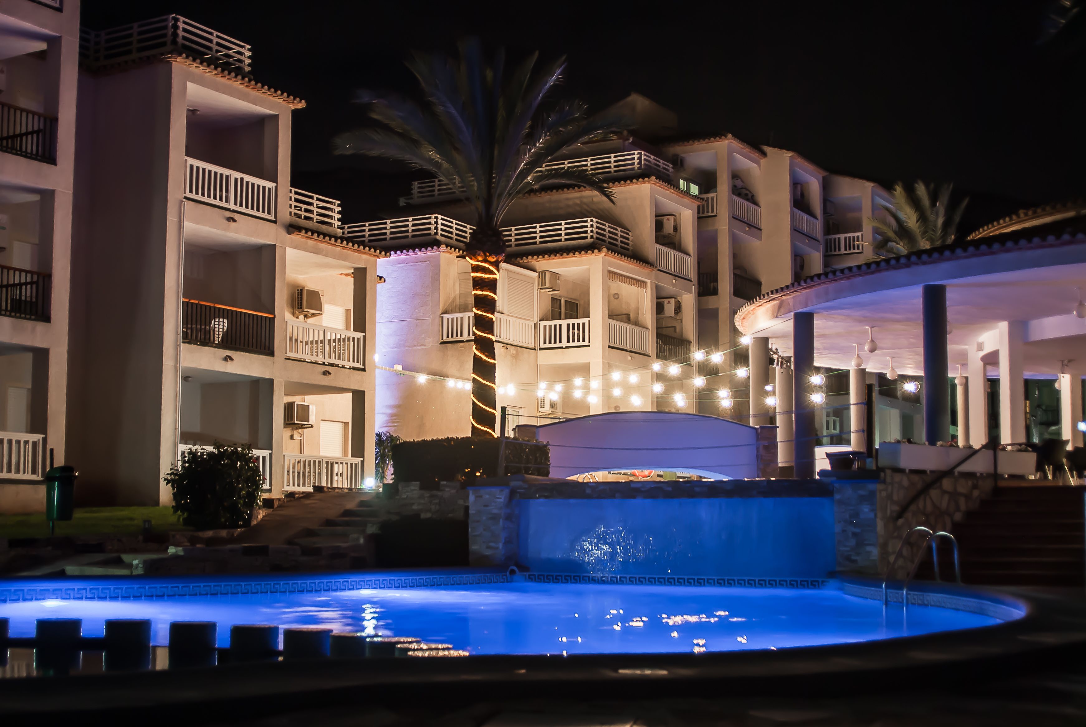 A multi-story hotel with balconies, a swimming pool, and outdoor lighting.