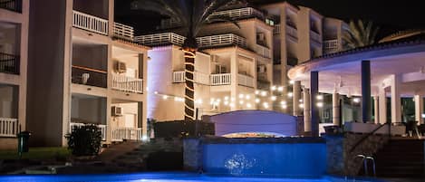 A multi-story hotel with balconies, a swimming pool, and outdoor lighting.