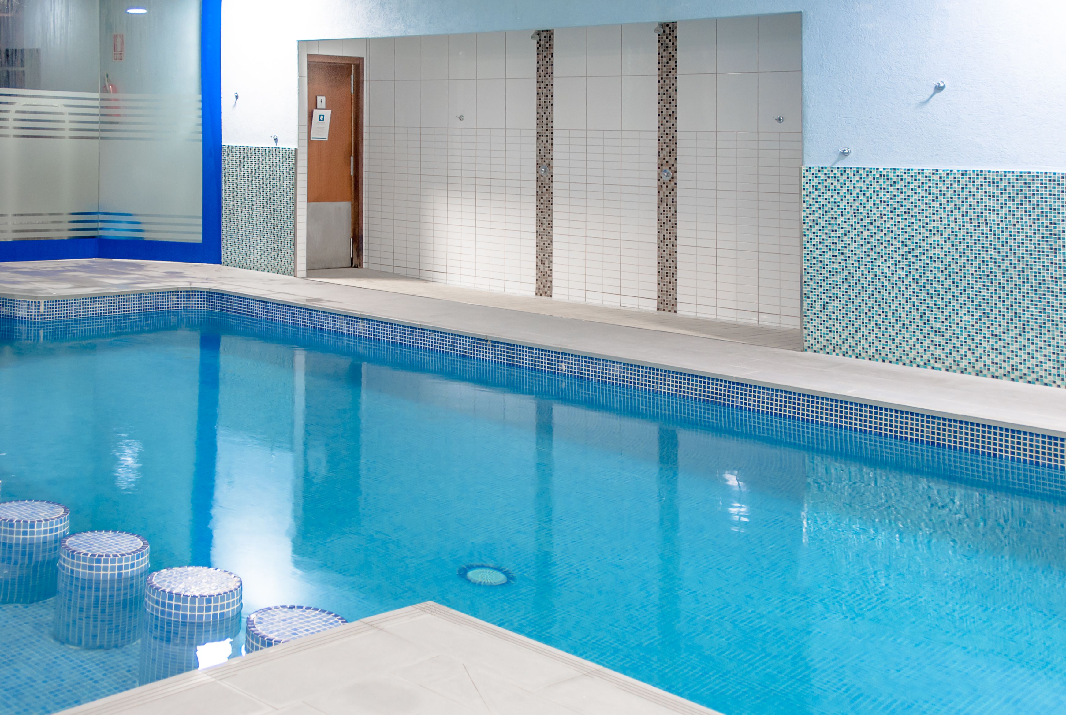Una piscina interior con agua cristalina, paredes y piso de baldosas.